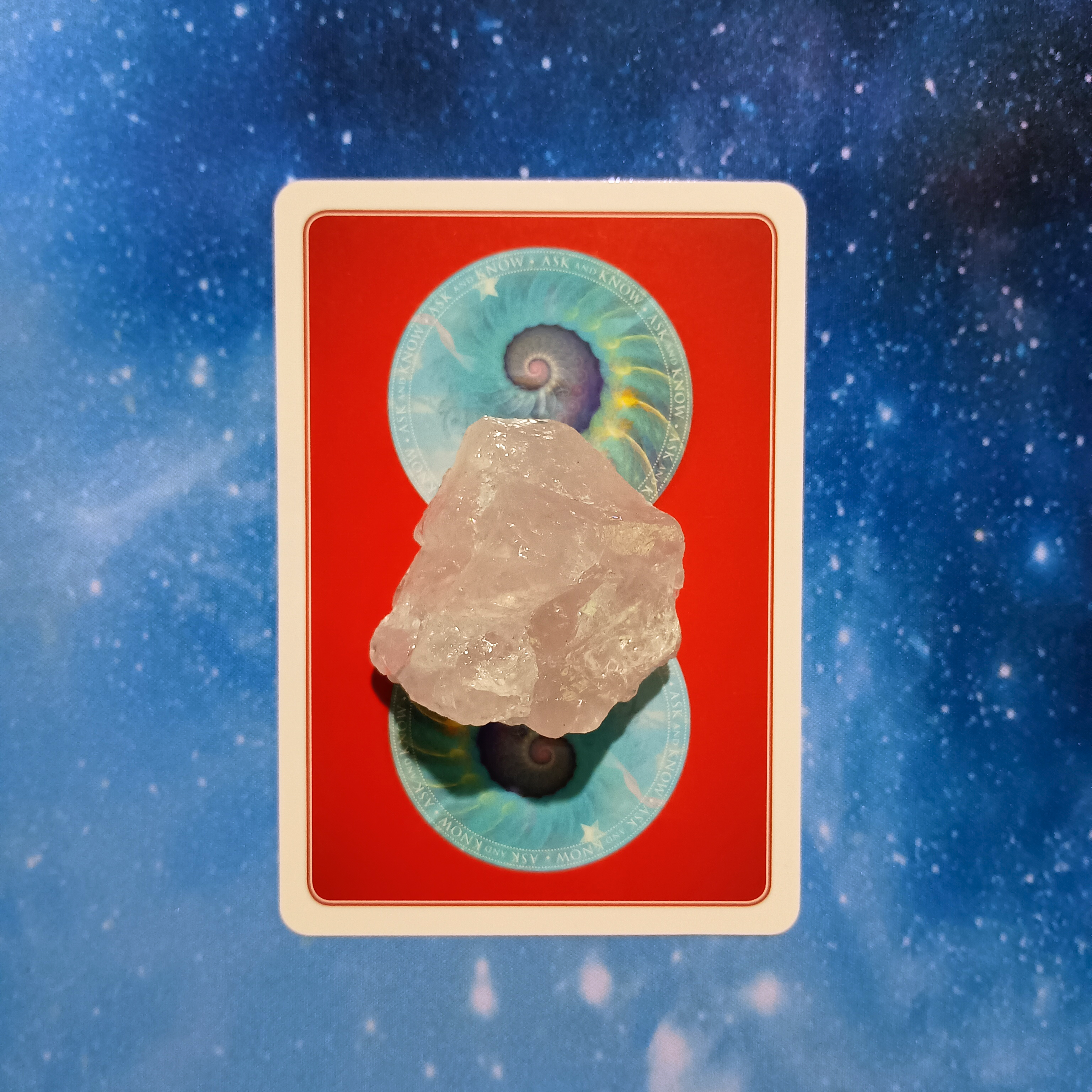 New Moon Pick-a-Card Tarot Reading for May 2025, pile 1 - rose quartz (pink) stone 
and an oracle card on a starry blue background