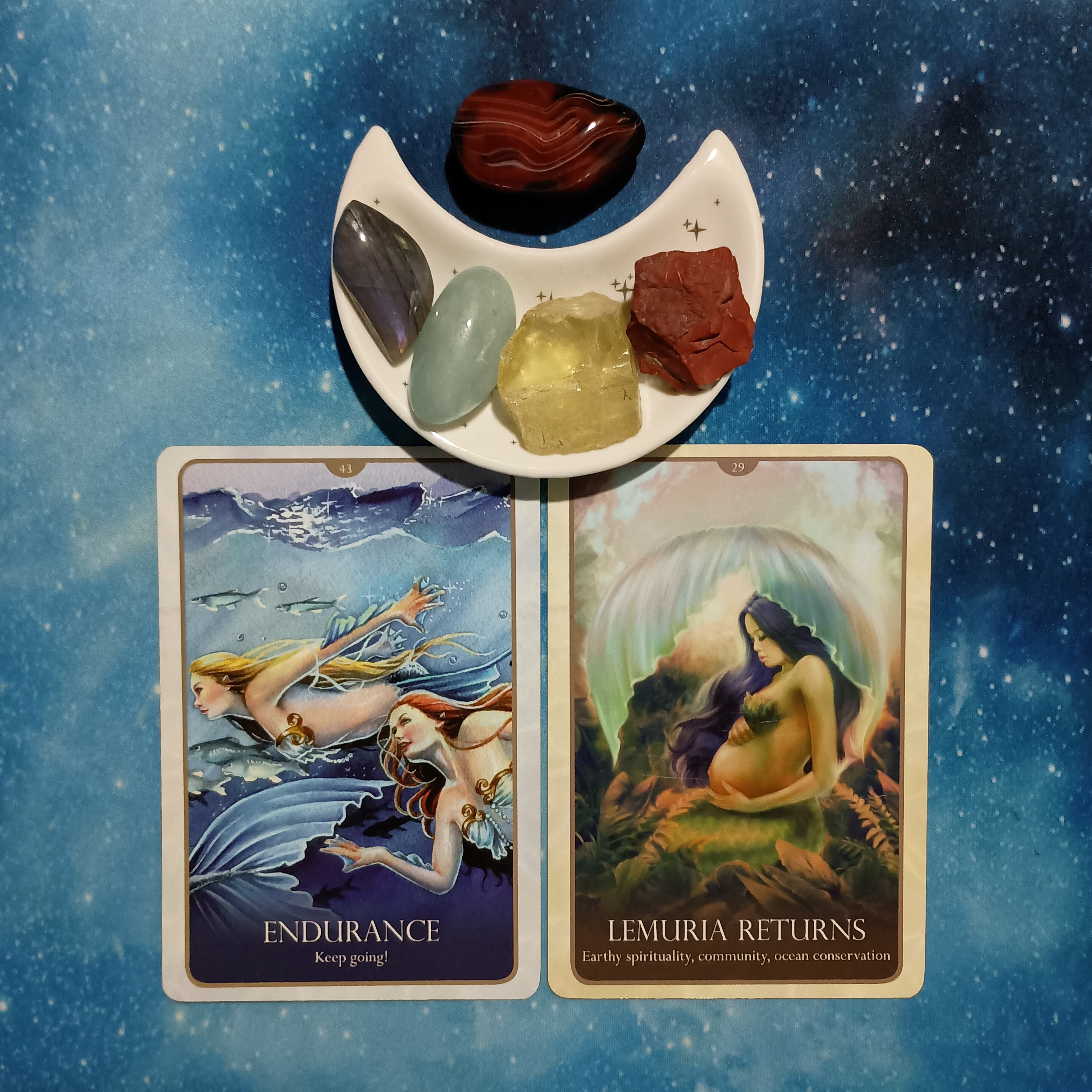 Care for Our Mother Earth ~ A Message From the Universe, two Oracle of the Mermaids cards and crystals on a starry blue background