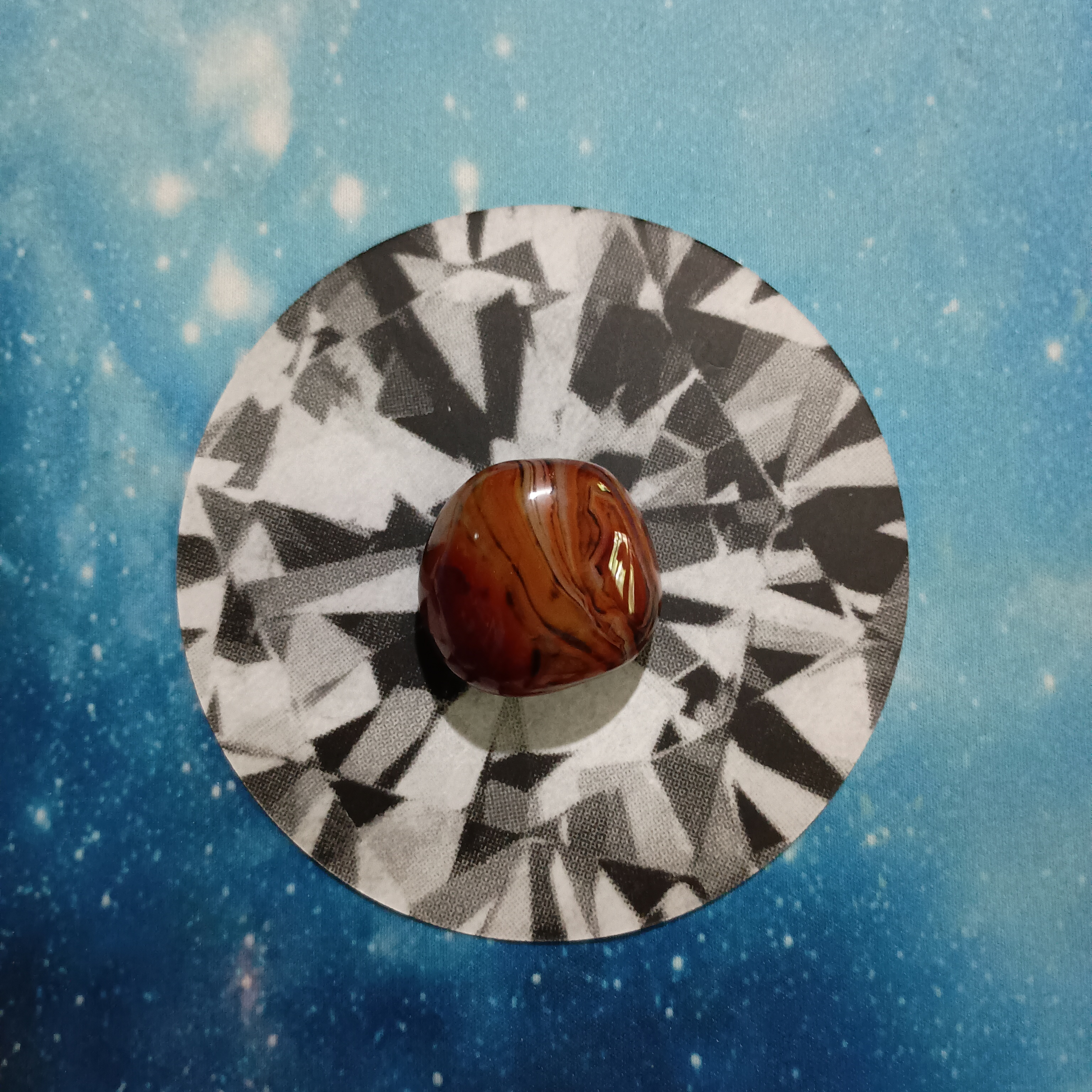 New Moon Pick-a-Card Tarot Reading for June 2025, pile 2 - Silk Agate stone (orange and brown) and an oracle card, face down, on a starry blue background
